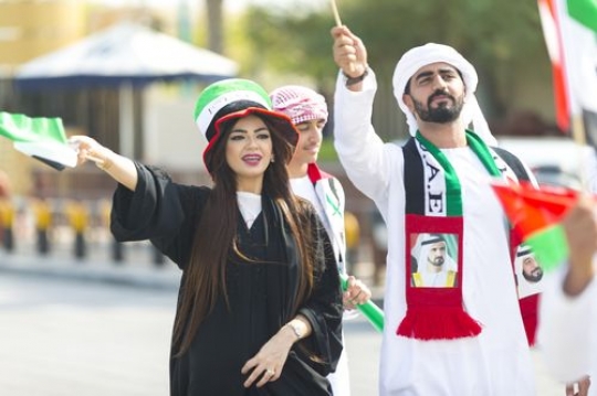 Arabian man and woman carrying UAE flags at a National Day parade|