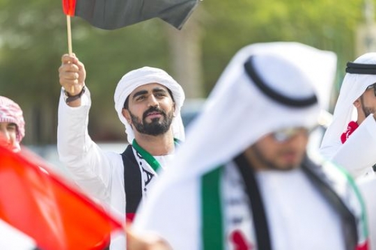 Arabian man carrying a UAE Flag at a National Day parade|