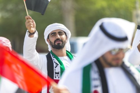 Arab man carrying a UAE Flag at a National Day parade|