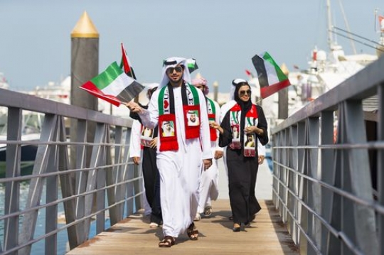 A group of people carrying UAE Flags during a National Day parade|