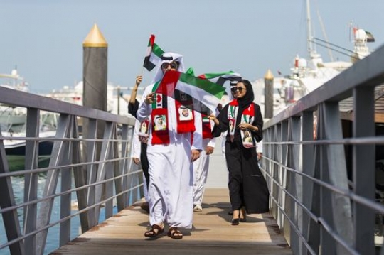 Arab family and friends walking on the dock carrying UAE flags celebrating National Day|