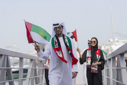 A group of people walking on the dock carrying UAE flags celebrating National Day|