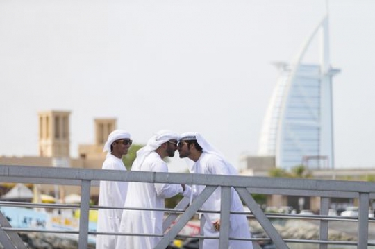 Men dressed in the traditional UAE attire standing by the dock saying hello in the traditional way|