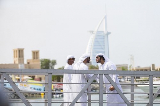 Men dressed in the traditional UAE attire standing by the dock greeting each other|