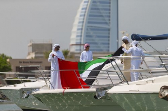 Arab men on a yacht holding a UAE flag to celebrate National Day|