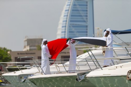 Arab men holding a UAE flag to celebrate National Day on a yacht|