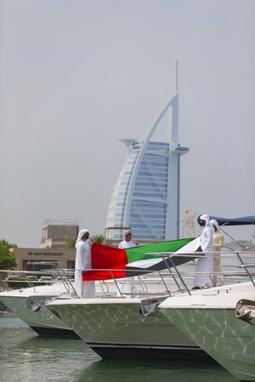 Arab men dressed in the traditional attire standing on a yacht holding a UAE Flag|