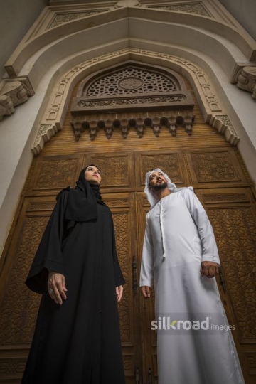 Middle Eastern Businessman and Businesswoman dressed in the traditional UAE attire standing next to each other|-