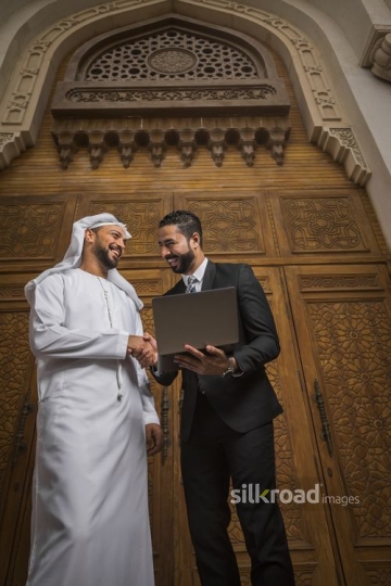 Middle Eastern Businessman carrying laptop shaking hands with his colleague|-