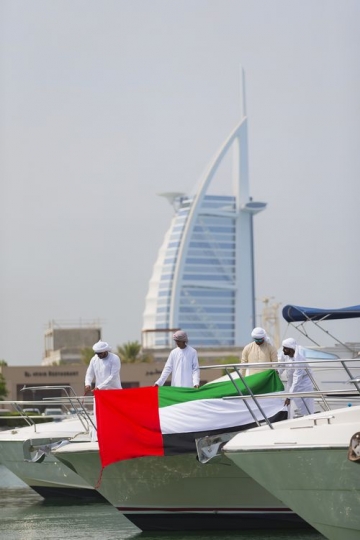 Men dressed in the traditional attire standing on the yacht holding a UAE Flag celebrating National Day|