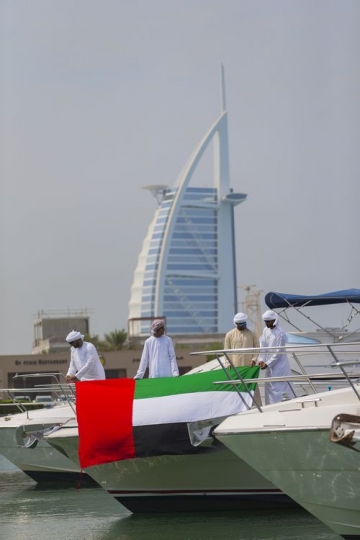 Men standing on the yacht holding a UAE flag celebrating National day|