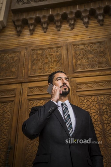 Middle Eastern Businessman standing using his mobile|-