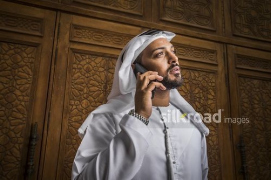 Medium shot of a Businessman dressed in the traditional UAE attire using his mobile|-