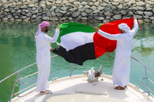 Two arab men standing on the yacht holding a UAE Flag|