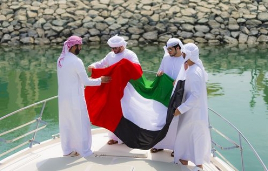 Four arab men standing on the deck of the yacht holding a UAE Flag|