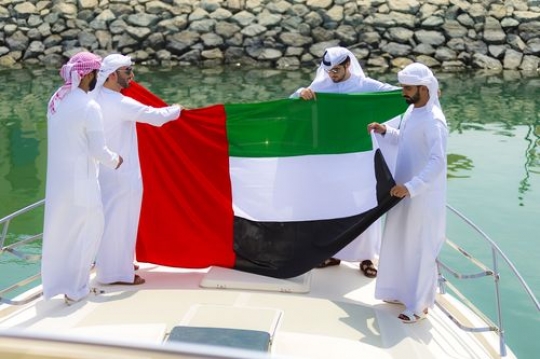 Arabian men holding the UAE Flag on the yacht|