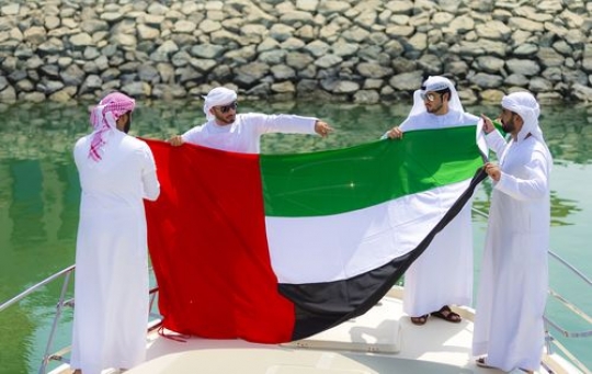 Men dressed in the traditional attire holding the UAE Flag on the yacht|