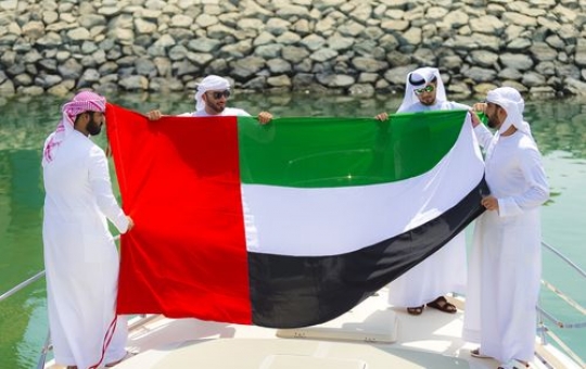 Arabian men dressed in the traditional attire holding a UAE Flag celebrating National Day|