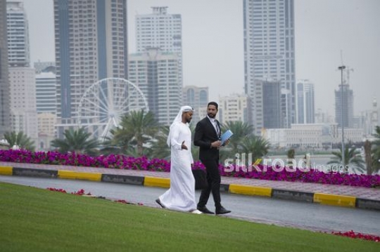 Middle Eastern Businessman dressed in the traditional UAE kandoura walking with his colleague dressed in a Business suit|-