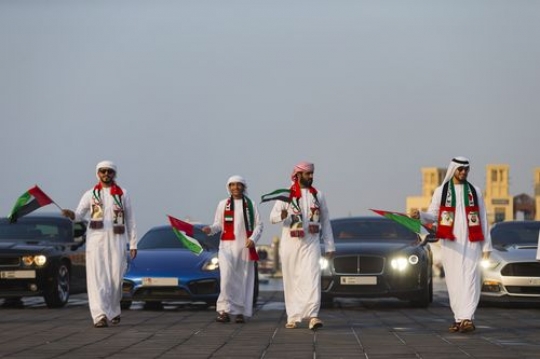 Arab men dressed in the traditional attire followed by luxury cars at National Day parade|