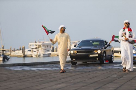 Arab men followed by black vehicle during a National Day parade|