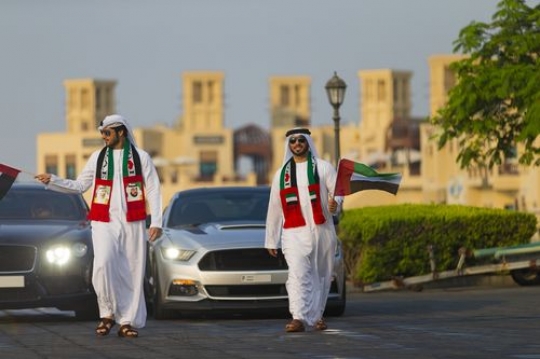 Arab men dressed in the UAE traditional attire followed by luxury cars at a National Day parade|