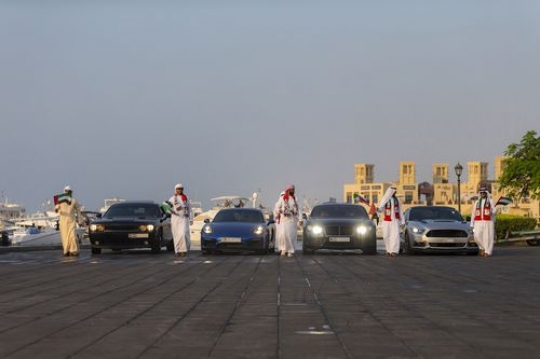 Arab men followed by luxury cars during a National Day Parade|-