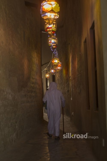 Middle Eastern man strolling through alley decorated with Ramadan lanterns|-