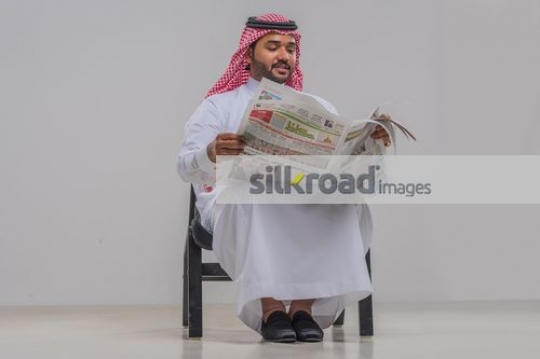 Middle Eastern man sitting on the chair reading the newspaper 
