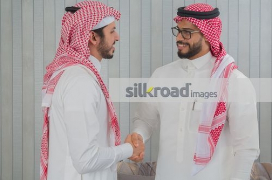 Middle Eastern Businessmen dressed in the traditional KSA attire shaking hands|