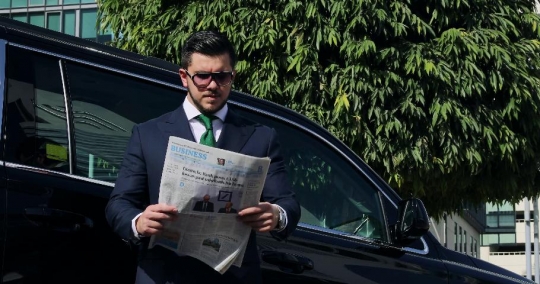 Western Businessman reading the newspaper next to his car|-
