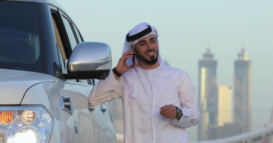 Middle Eastern man leaning on the car talking on the phone|-