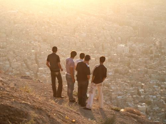 young men standing on a cliff looking at the city