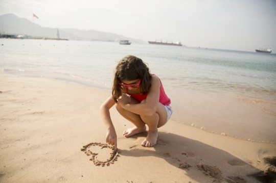 Little Girl Drawing Heart Shape in Sand