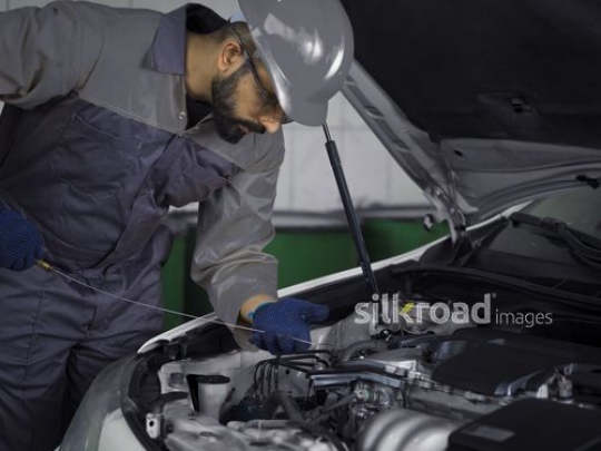 Mechanic worker dressed in uniform checking the oil of the car|-
