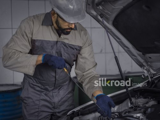 Worker dressed in uniform checking the oil of the car