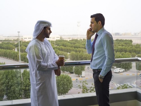 Two businessmen outdoors one is on the phone and the other one is holding a coffee