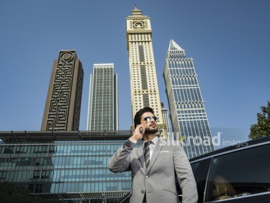 Businessman standing wearing his sunglasses using his phone|-