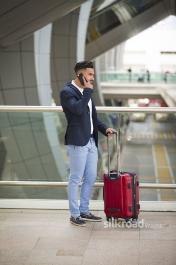 Arab man standing with his luggage using his mobile|-