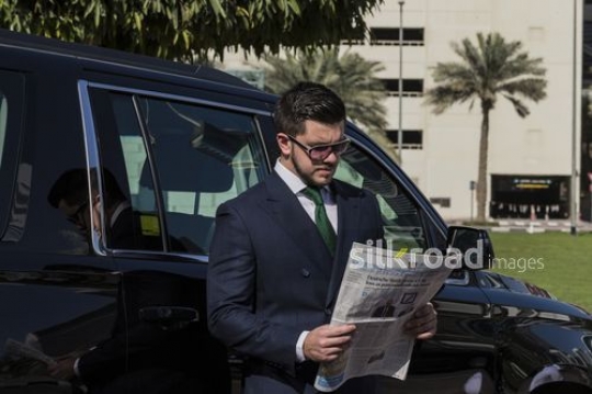 Businessman standing infront of his car reading a newspaper |-