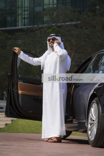 Arab Businessman standing by his car talking on the phone|
