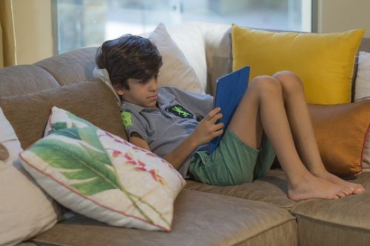 Middle eastern boy sitting on the couch playing on his device|-