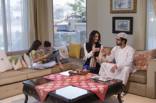 Arab mother giving her husband coffee while the kids are on their devices|-