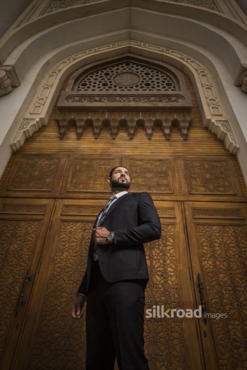 Arab Businessman standing infront of a brown gate|-