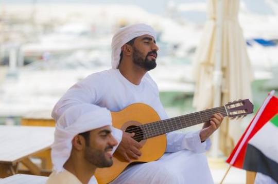 Arab man playing an instrument while singing a song for national day|