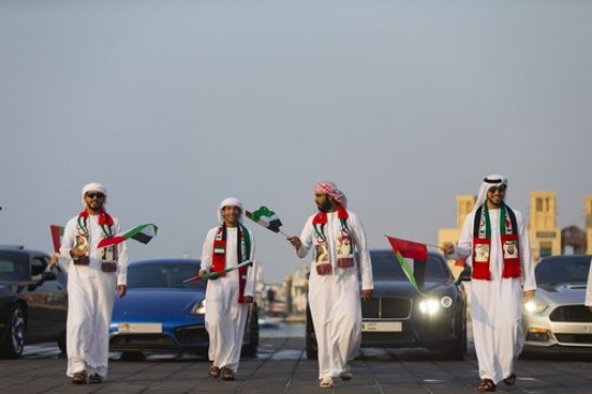 A group of men dressed in the UAE traditional attire followed by luxurious vehicles at National Day parade|