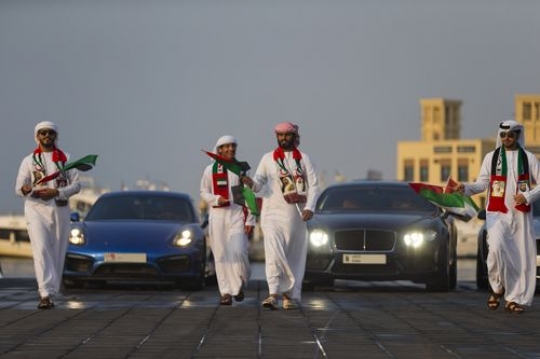 Arab men dressed in the traditional attire followed by luxurious vehicles during a National Day parade|