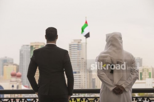 Middle Eastern men standing next to each other with the UAE Flag between them|-