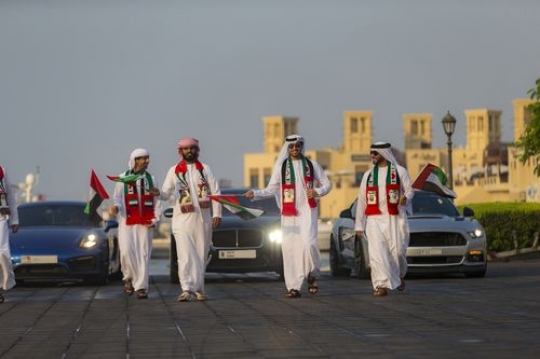 Middle eastern men dressed in the traditional attire followed by luxurious cars during the national day parade|-