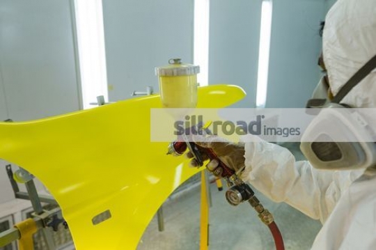 Worker painting the part of the car the color yellow|